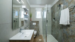 A modern bathroom with a large mirror, a sink, a toilet, and a shower area. - Hacienda Afrodita by Villas Guide (Loborika)