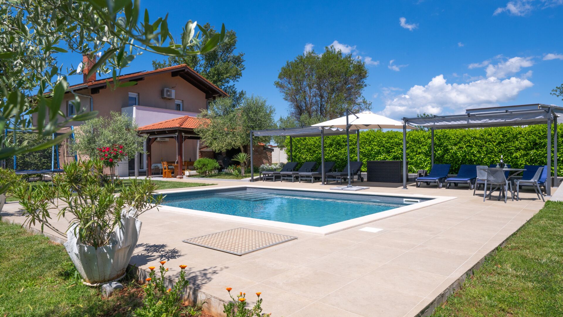 A swimming pool with lounge chairs, a covered patio, and a house with a red roof.