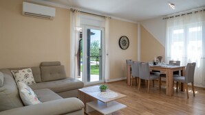 Een woonkamer met een bank, een eettafel met stoelen, een salontafel en een klok aan de muur.