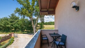 A balcony with a table and chairs, a view of trees and a field, and a wall-mounted light fixture. - Hacienda Afrodita by Villas Guide (Loborika)