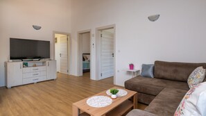 A living room with a brown sofa, a wooden coffee table with a plant, a TV on a white cabinet, and a door leading to a bedroom. - Hacienda Afrodita by Villas Guide (Loborika)