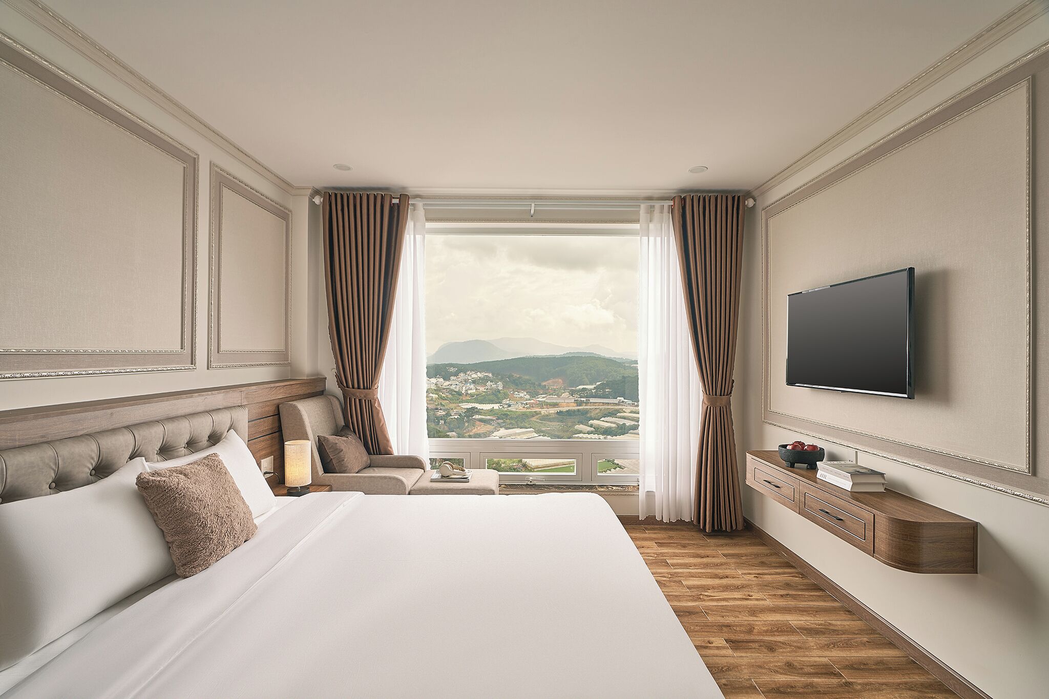 Ein Hotelzimmer mit einem großen Bett, einem Fernseher, einem Schreibtisch mit Schubladen und Blick auf die Landschaft.