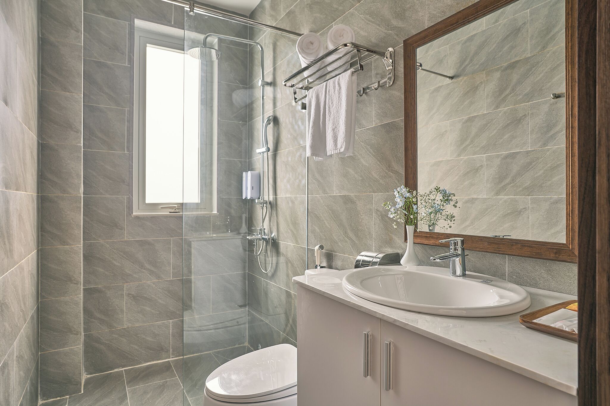 A modern bathroom with a glass-enclosed shower, a large mirror, and a white sink.