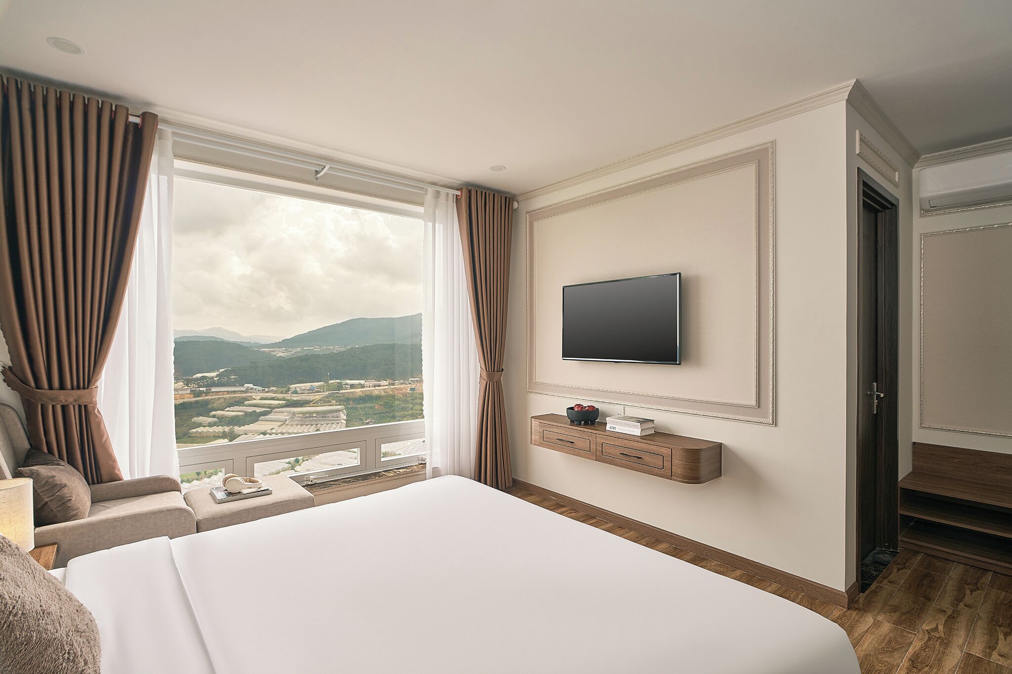 A hotel room with a large bed, a TV mounted on the wall, a small bedside table, and a view of the mountains through the window.