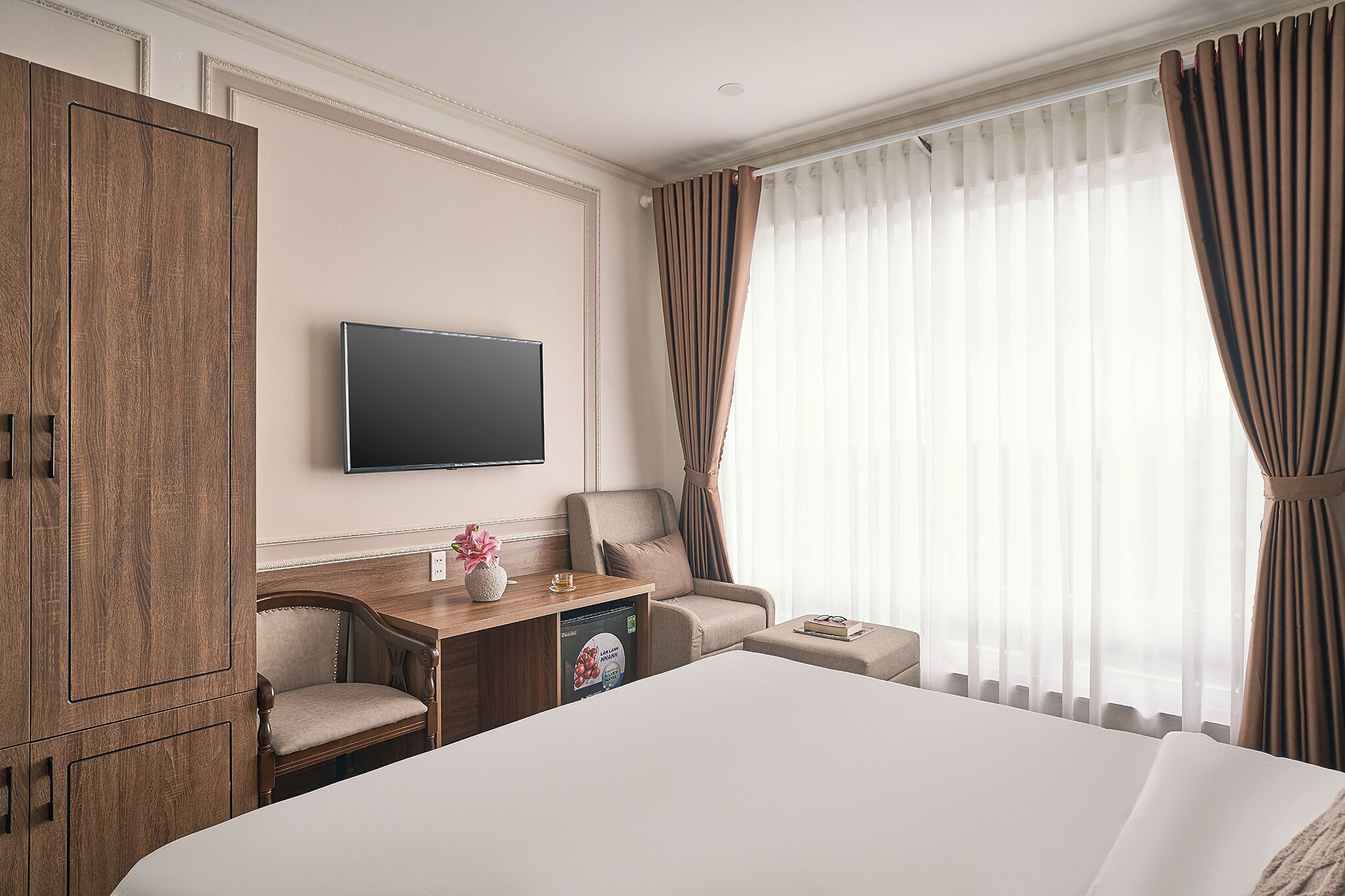 A hotel room with a large bed, a wooden desk with a television, a chair, and a sofa.