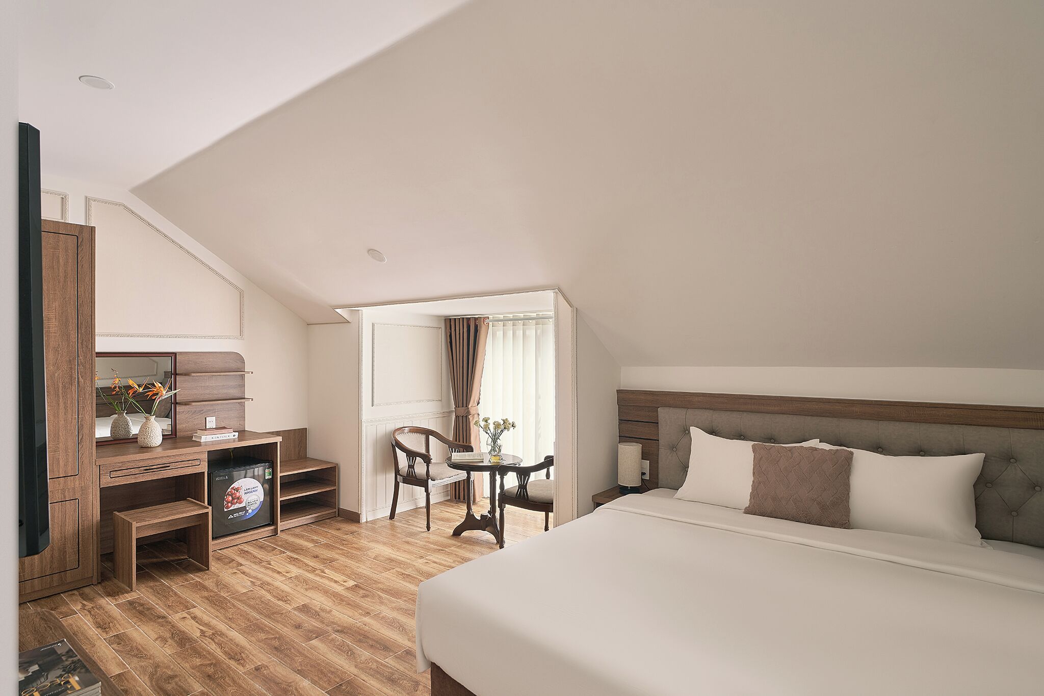 A hotel room with a bed, a desk, a chair, and a small table with a vase.