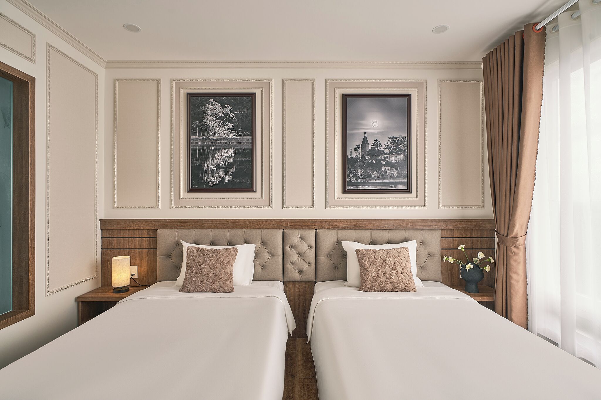 A hotel room with two beds, a nightstand with a lamp, and two framed pictures on the wall.