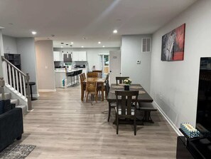 Una sala de estar moderna con comedor, cocina al fondo y una escalera que sube a otro nivel.