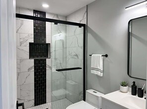 Un baño moderno con cabina de ducha de vidrio, un lavabo blanco, un inodoro y un espejo.