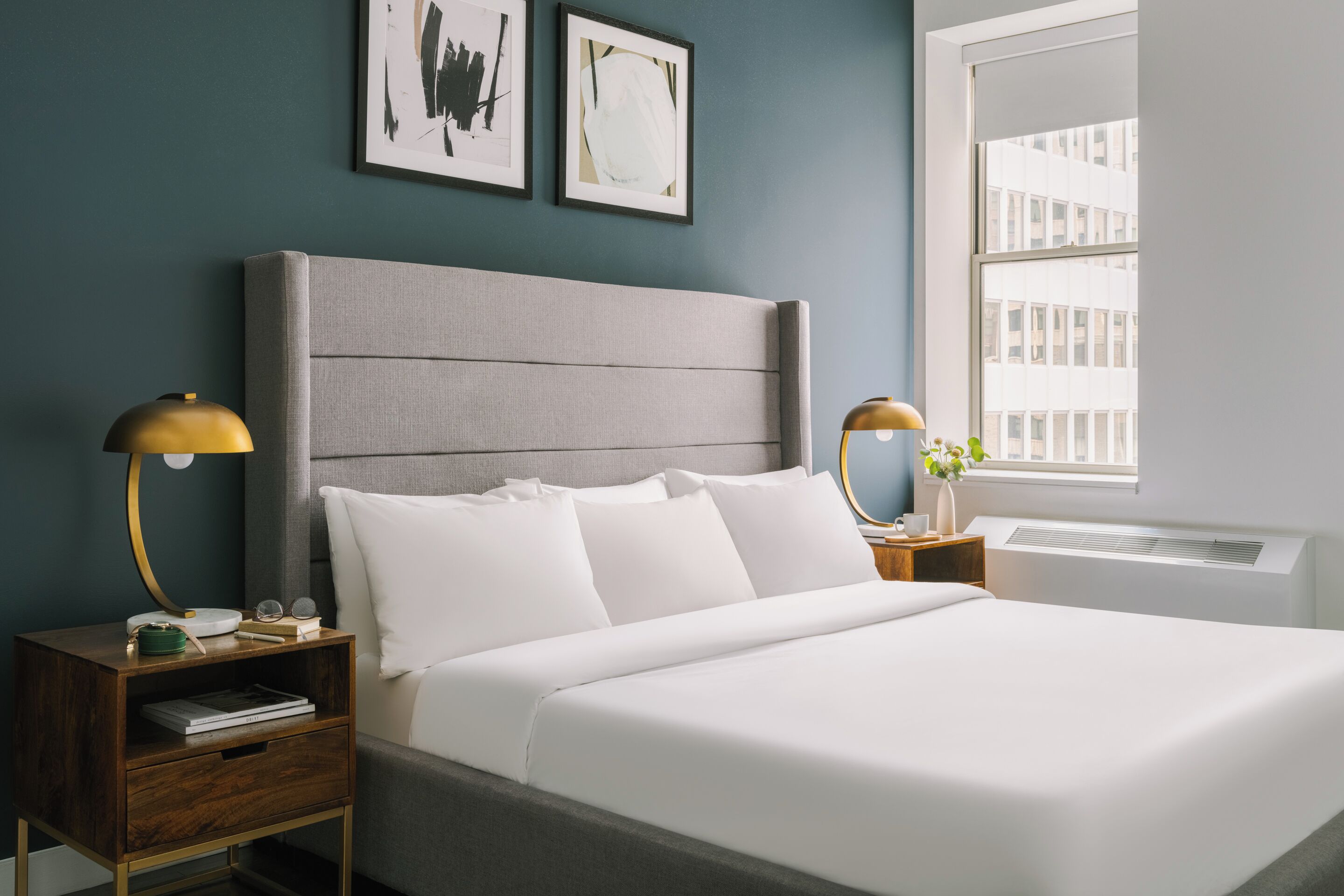 A neatly made bed with white linens, a grey upholstered headboard, and two bedside tables with lamps.