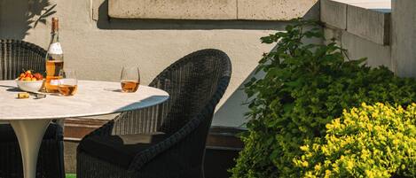 A rooftop terrace with a table, chairs, a bottle, and glasses, overlooking a cityscape with modern buildings.