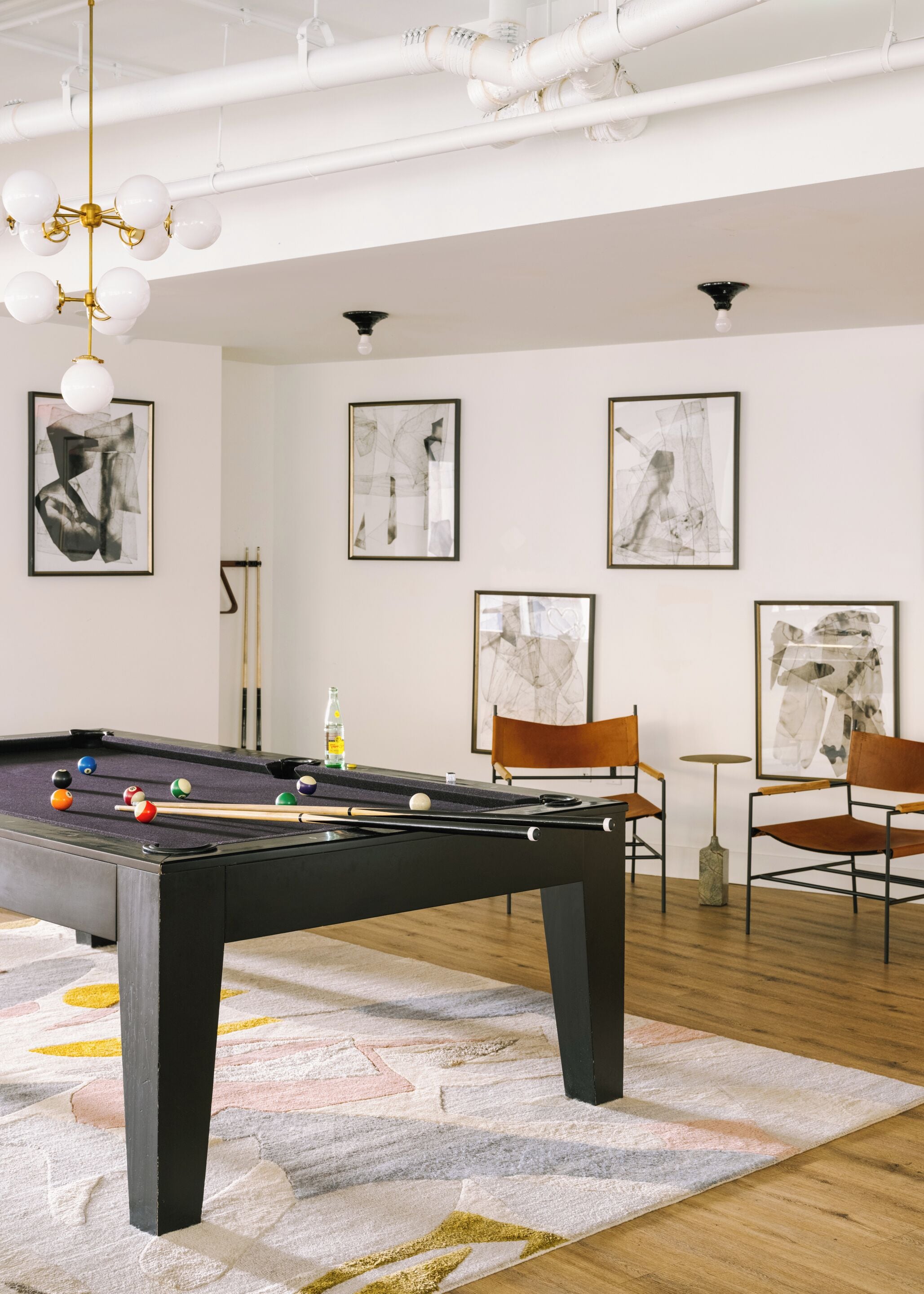 Una mesa de billar en una habitación con paredes blancas, arte abstracto y sillas modernas.