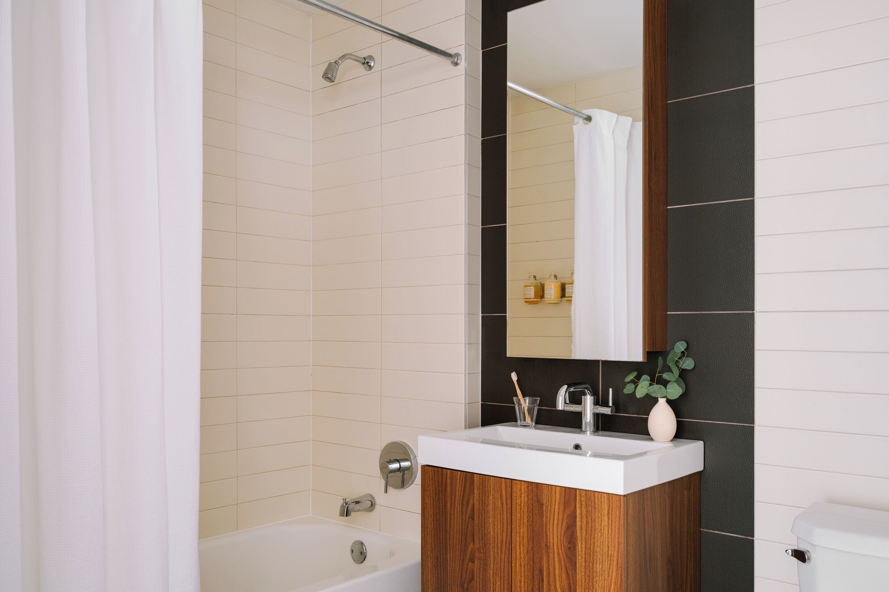 A modern bathroom with a white bathtub, wooden vanity, and a large mirror.