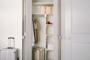 A white closet with hanging clothes, a suitcase, and a shelf with folded towels.