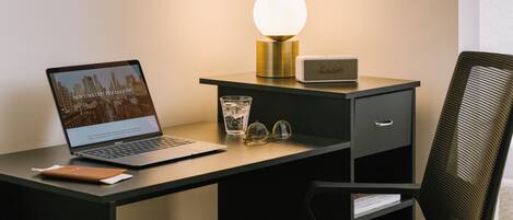 A laptop on a desk with a lamp, a glass of water, and a pair of glasses.