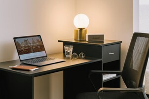 Una computadora portátil sobre un escritorio con una lámpara, un vaso de agua y un par de lentes.