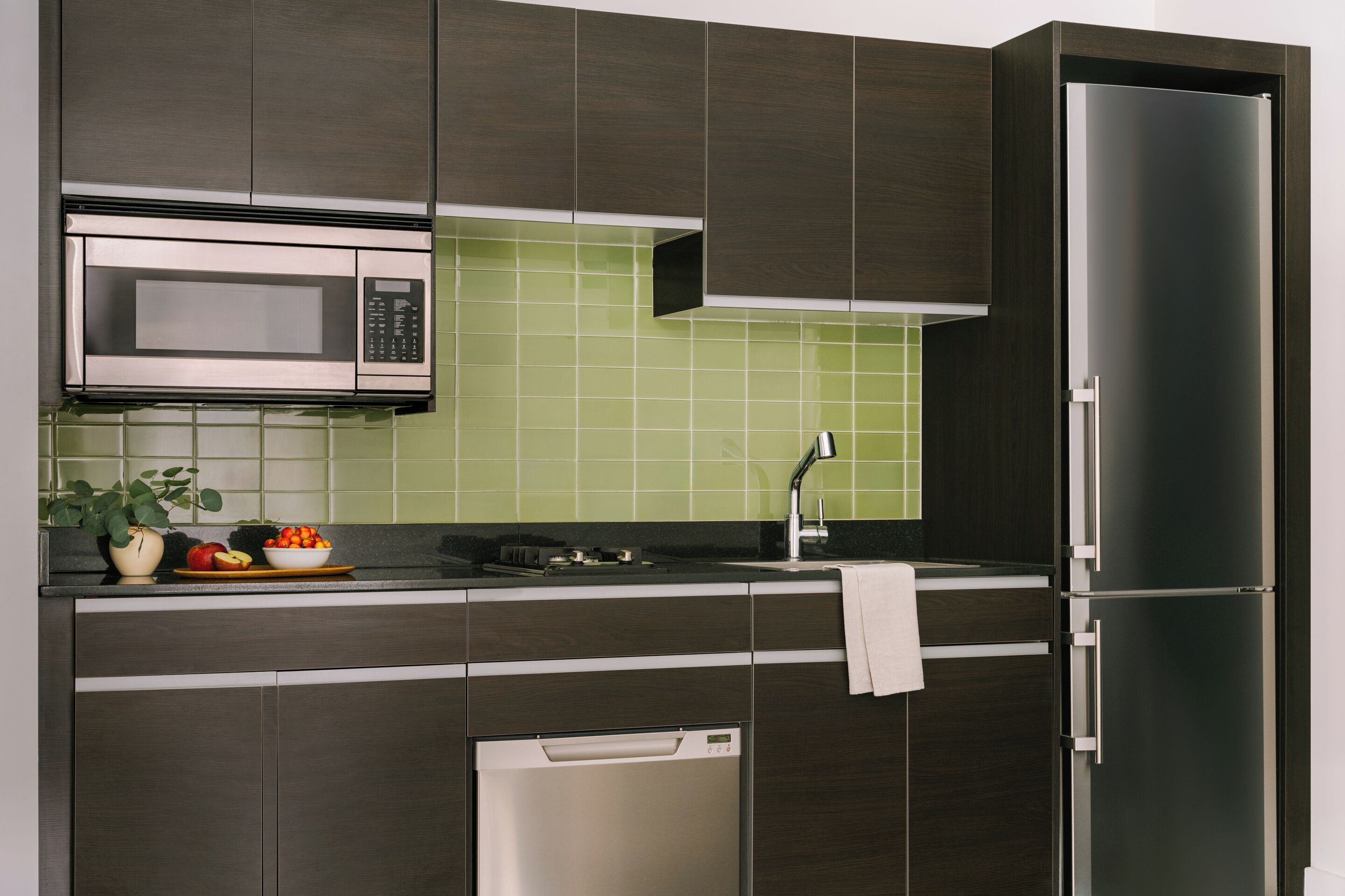 Uma cozinha moderna com armários escuros, um micro-ondas de aço inoxidável e uma geladeira.