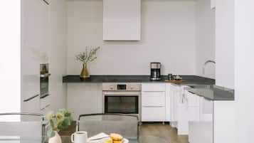 A modern kitchen with white cabinets, a black countertop, a built-in oven, and a dining area with a glass table and chairs.