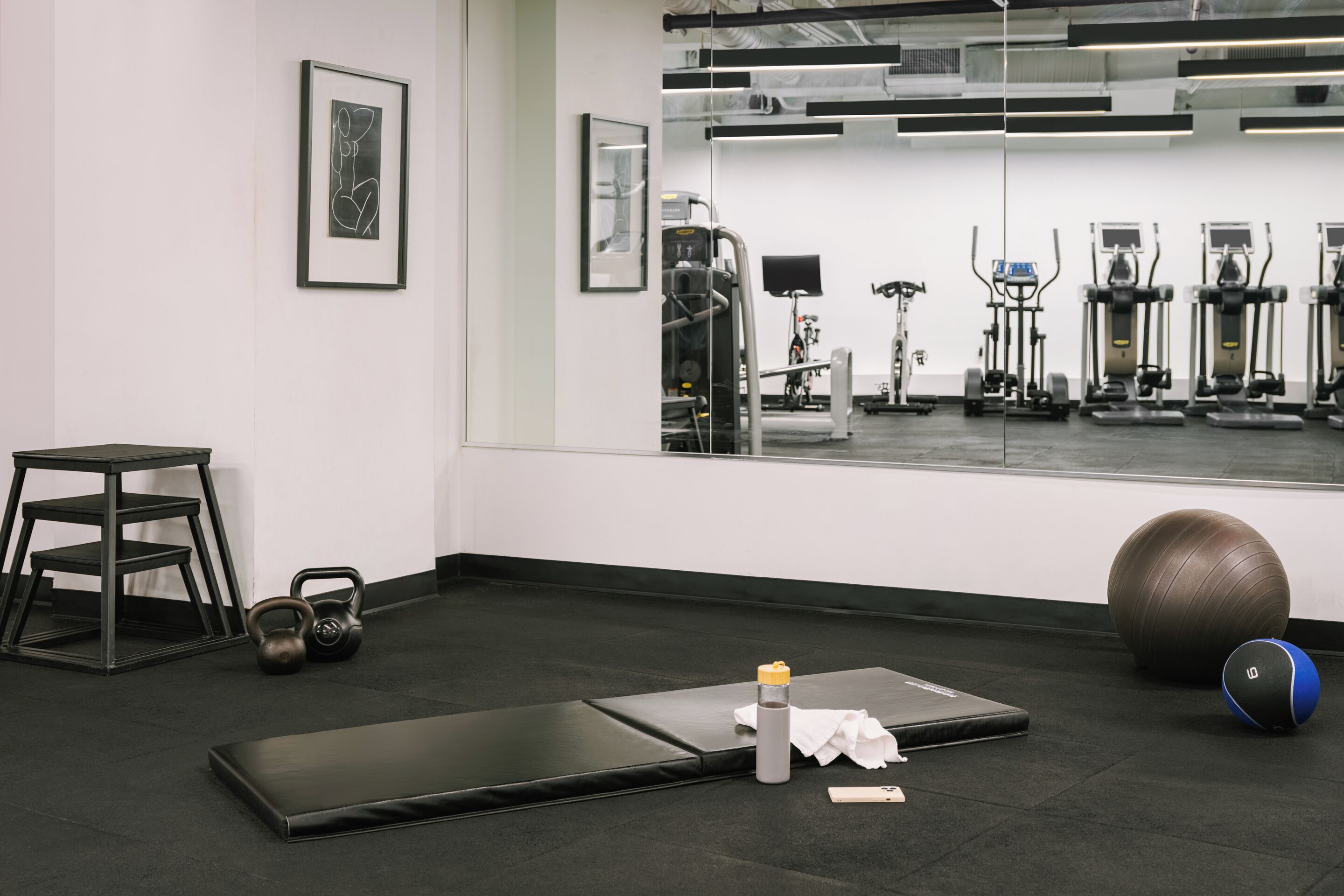 Une salle de sport équipée de matériel d’exercice, d’un kettlebell, d’un tapis et d’une bouteille d’eau.