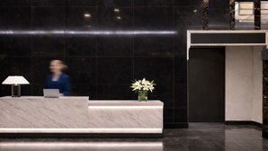 En receptionsdisk med en bärbar dator, en vas med blommor och en person i bakgrunden.