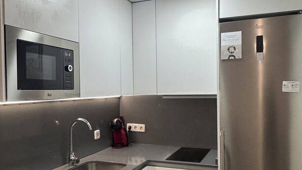 Una cucina compatta con microonde integrato, frigorifero in acciaio inox, lavatrice e lavello.