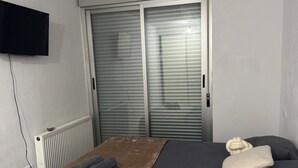 Una camera da letto con un letto, una televisione a schermo piatto montata a parete e una finestra con persiane.