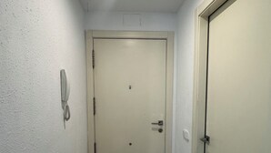 Un corridoio stretto con una porta bianca in fondo, un lampadario a soffitto e un telefono fissato al muro.