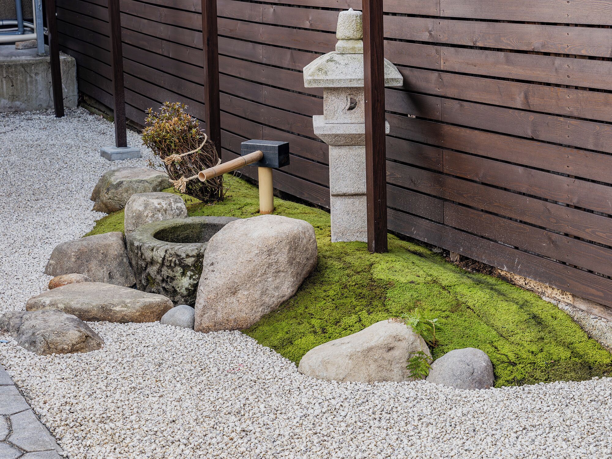 A traditional Japanese garden with a stone lantern, a wooden post, and a rake.