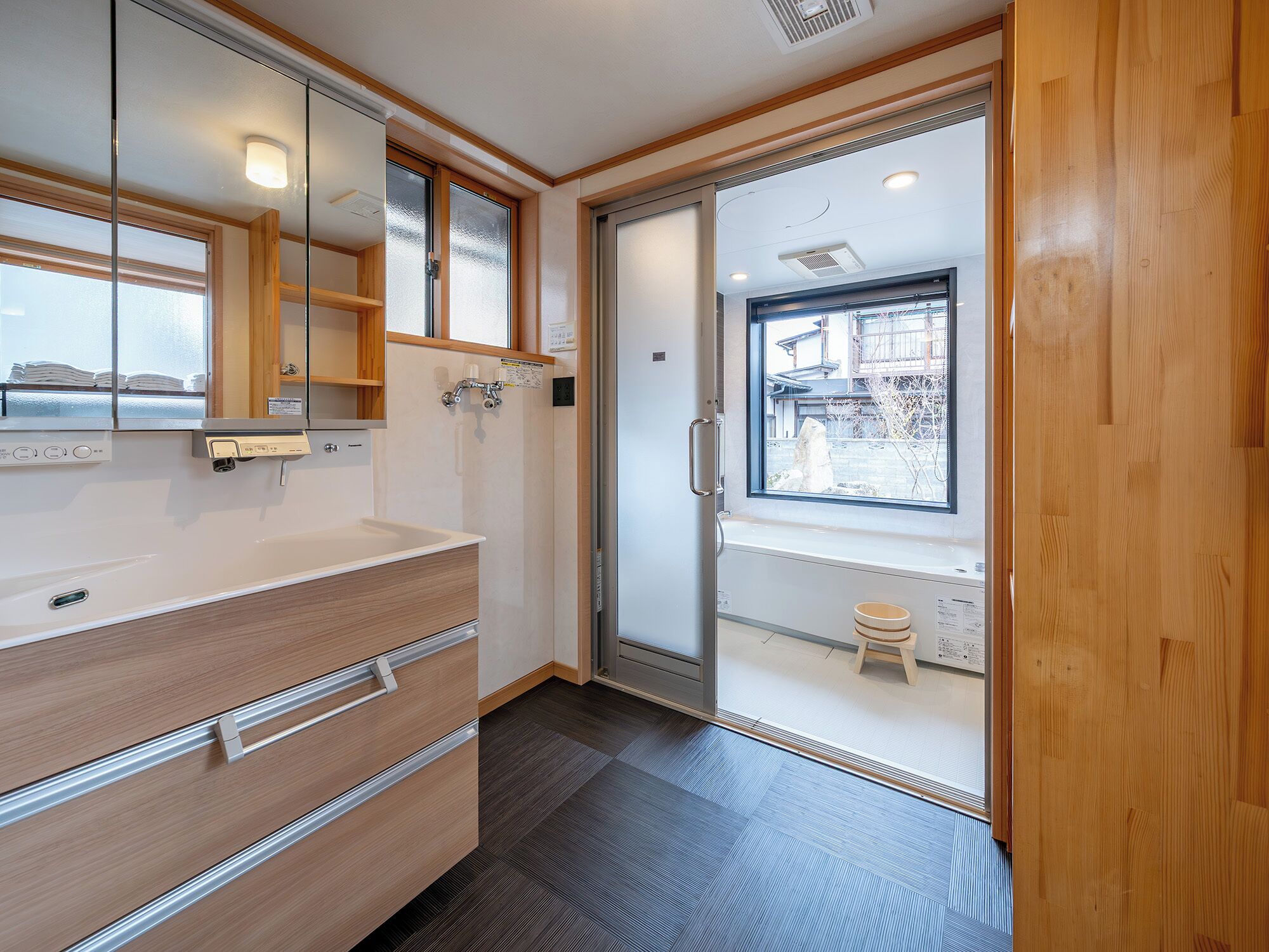 A modern bathroom with a large mirror, wooden vanity, and a window providing a view of the outside.