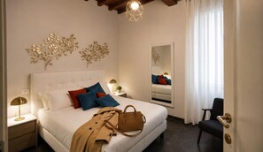 A hotel bedroom with a bed, bedside lamps, a mirror, a chair, and a coat on the bed. - Red Door Dream Apt. 5 (Firenze)