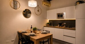 A modern kitchen with white cabinets, a microwave, and a dining area with a wooden table set for two. - Red Door Dream Apt. 5 (Firenze)