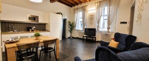 A modern kitchen with a microwave, stove, and dining area. There is a TV in the living room with a sofa and a plant. - Red Door Dream Apt. 5 (Firenze)