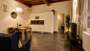 A modern living room with a dining area, a kitchen with white cabinets, a TV, and a fireplace. - Red Door Dream Apt. 5 (Firenze)