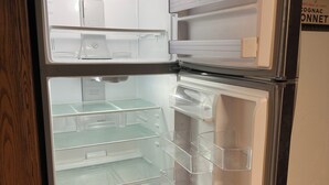 Avoin jääkaappi, jossa on useita hyllyjä ja laatikoita, vasemmalla puolella puinen kaappi ja lattialla laatat.