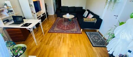 A living room with a sofa, a coffee table, a TV, a laptop, and a dining table.