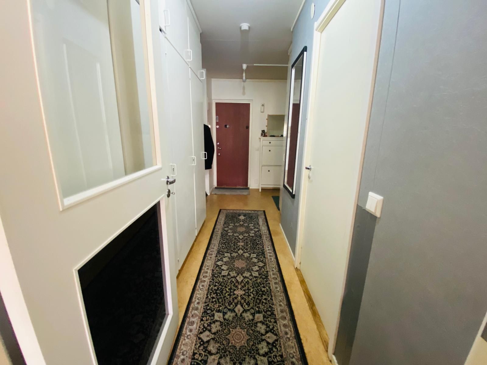A hallway with a patterned rug, a door with a black handle, and a white cabinet.