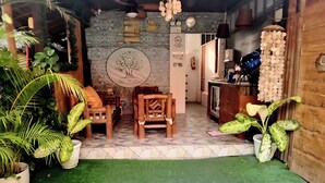 A cozy room with a stone wall, a wooden door, and a small table with chairs. There are potted plants and a hanging light fixture. - MJs Garden Hotel Moalboal powered by Cocotel (Moalboal)
