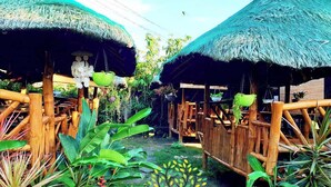 A rustic outdoor setting with thatched-roof structures, bamboo furniture, and lush greenery. - MJs Garden Hotel Moalboal powered by Cocotel (Moalboal)