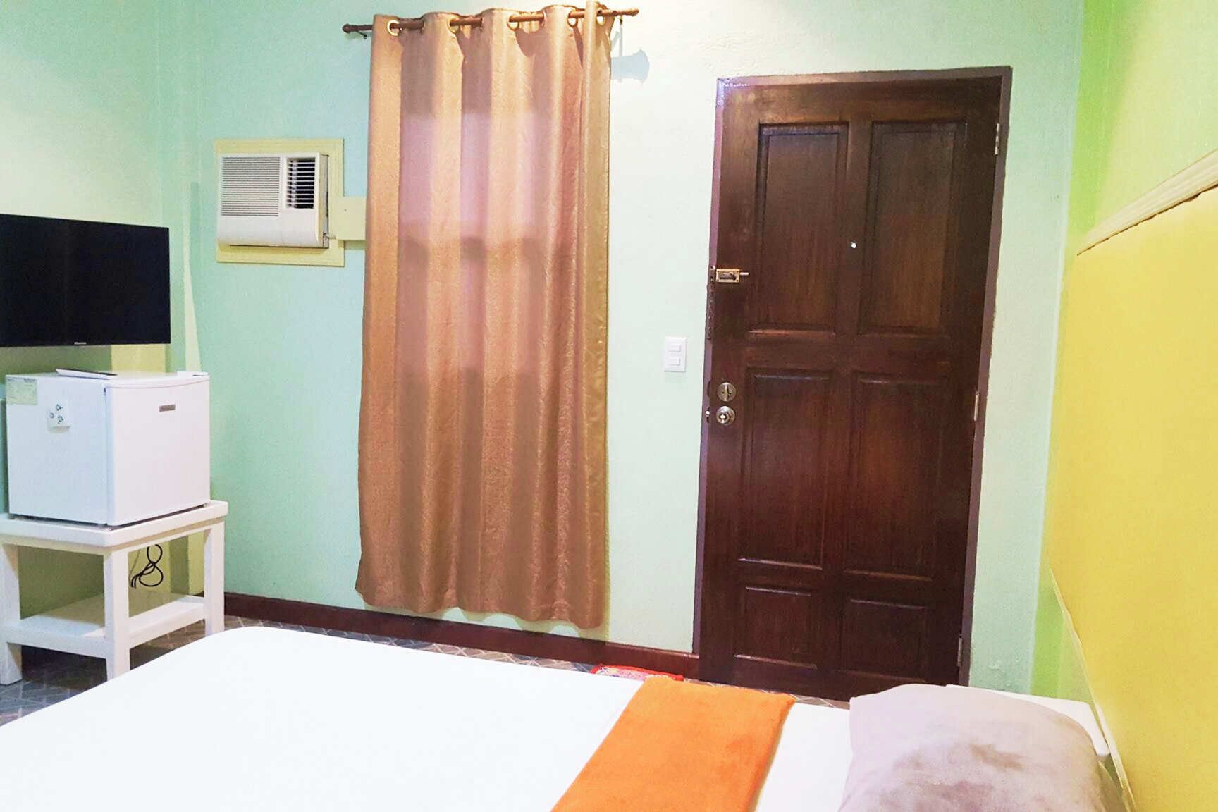 A room with a bed, a white refrigerator, a brown door, and a curtain.