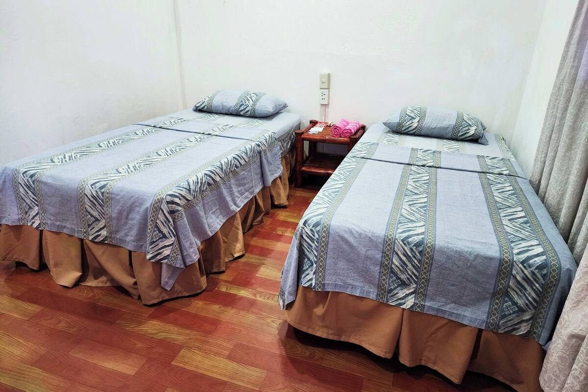 Ein Zimmer mit zwei Betten, jedes mit gemusterten Betttextilien und einem dazwischenliegenden Nachttisch.