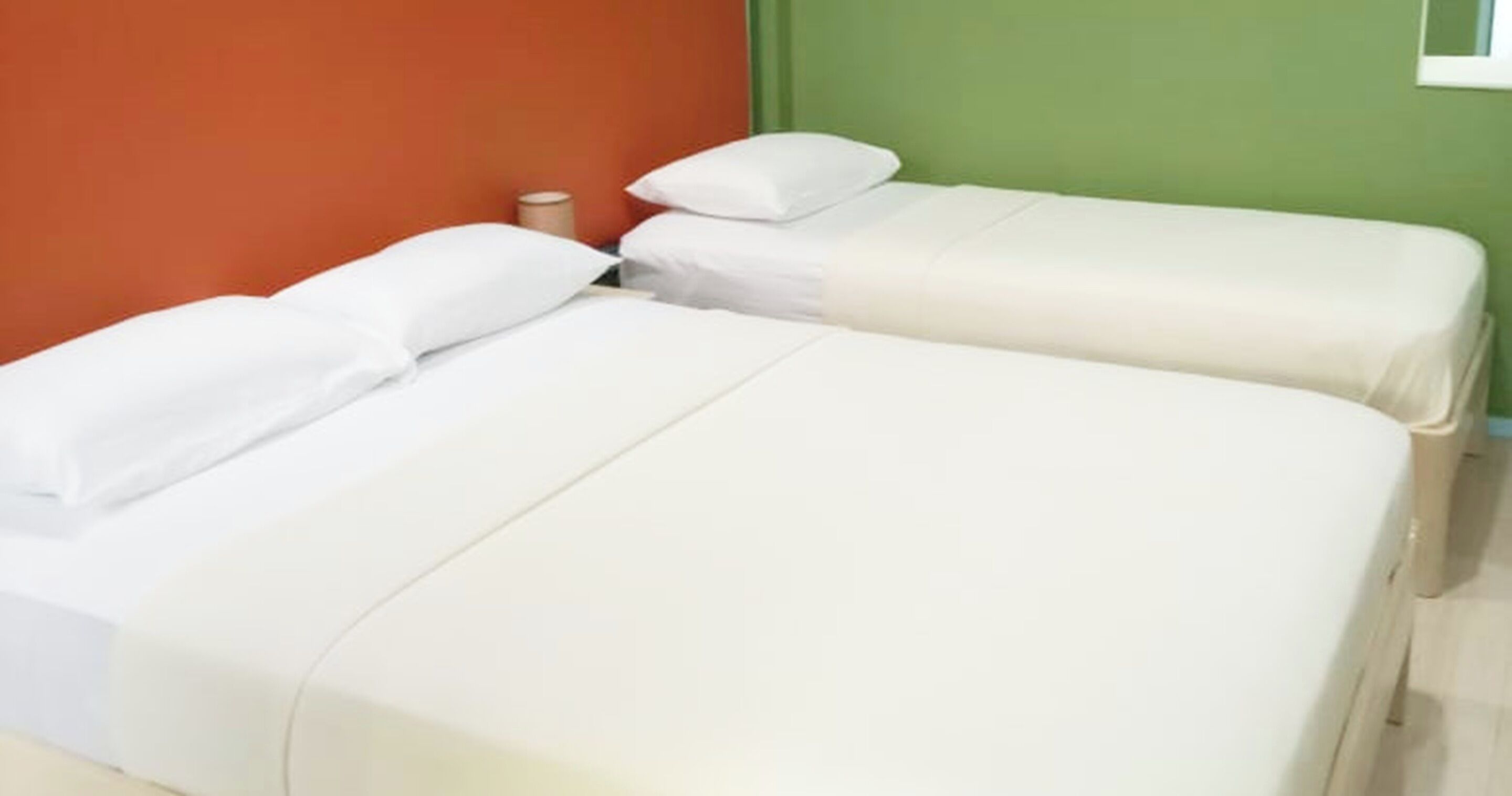 Two single beds with white linens in a room with green and orange walls.