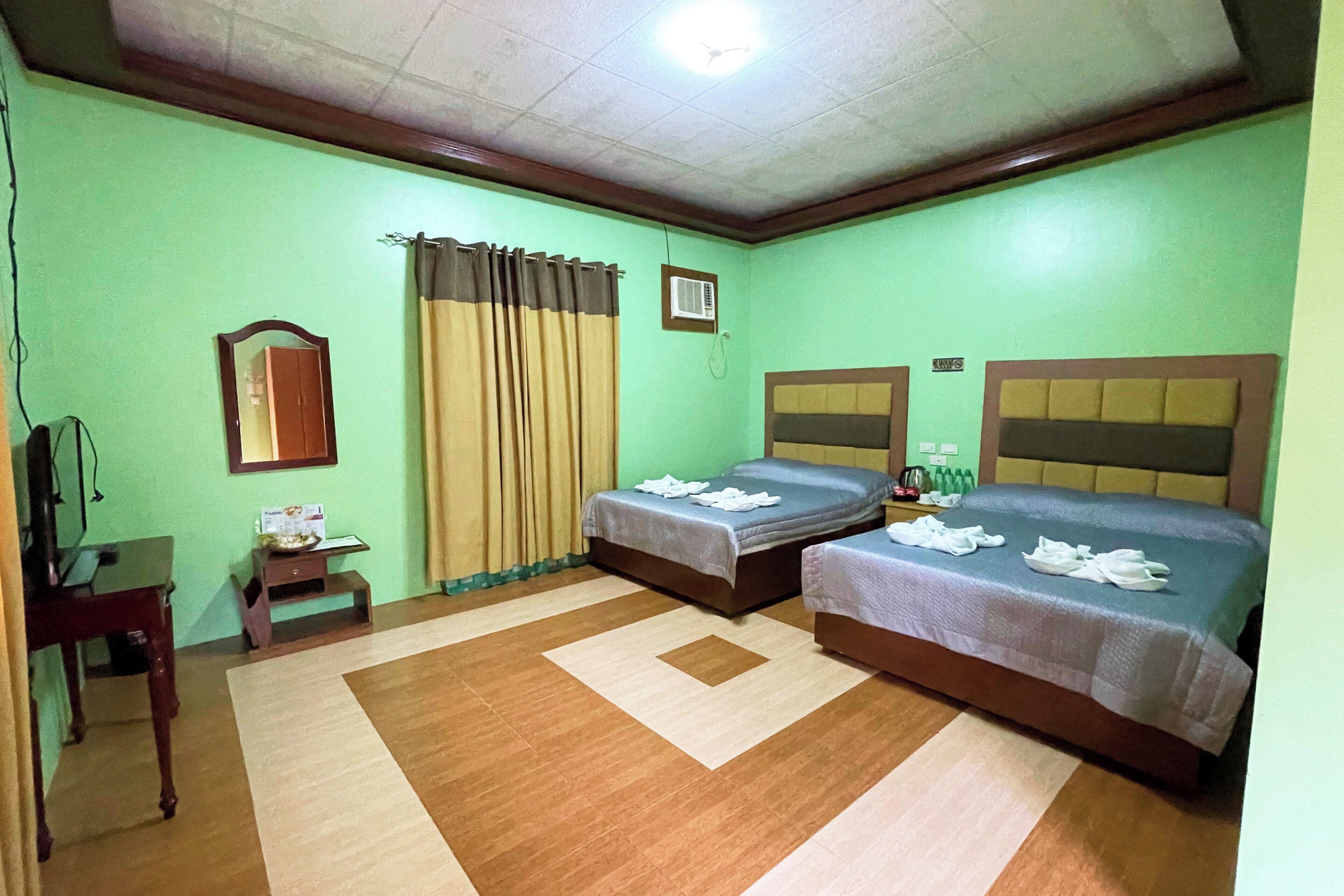 A hotel room with two beds, a desk, a chair, a mirror, and a window with curtains.