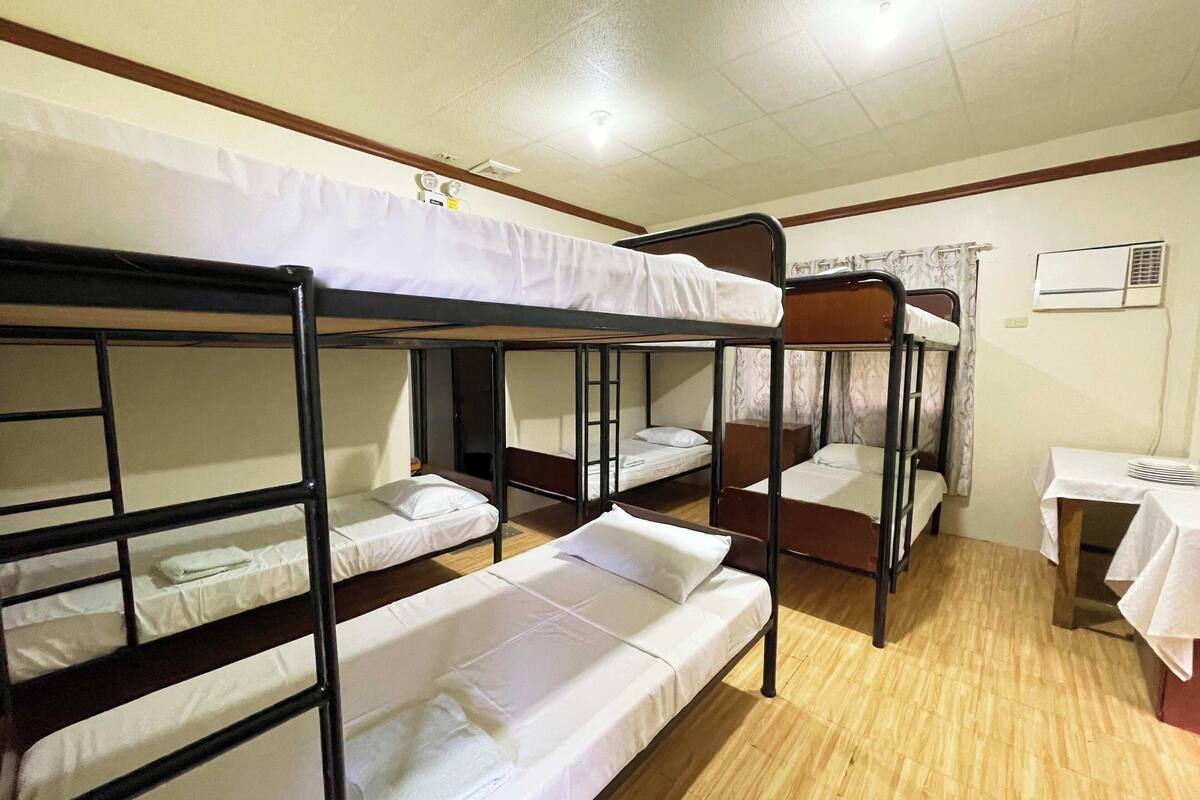 Un dormitorio con literas, una mesa pequeña con mantel y un equipo de aire acondicionado en la pared.