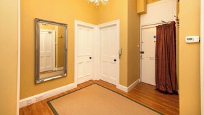 A hallway with a chandelier, a mirror, two white doors, a brown curtain, and a thermostat on the wall.
