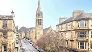 A street view with historic buildings, a prominent church tower, and parked cars along the road.