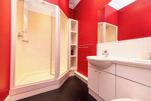 Ein Badezimmer mit Bodendusche, weißen Schränken und einer roten Akzentwand.