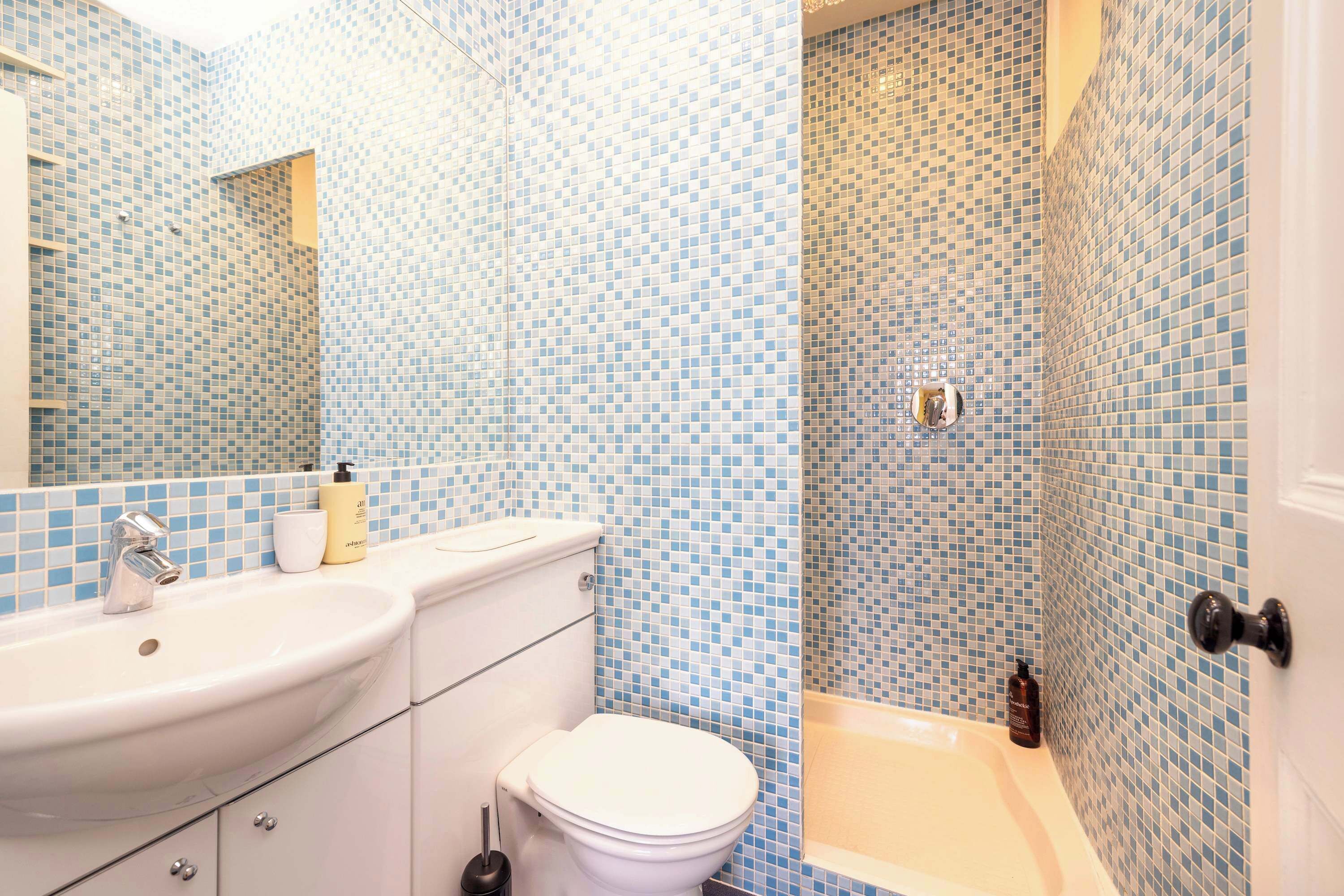 A bathroom with a sink, toilet, and bathtub, all with blue mosaic tile walls.
