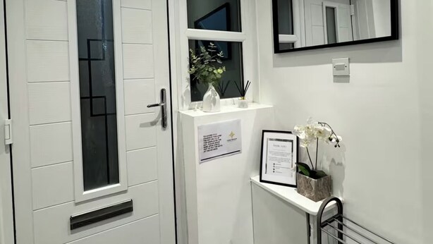 A clean, white interior with a door, a window, a mirror, and a small shelf with decorative items. - Contractor/Corporate-Friendly Home | Sleeps 6 | Long Stays (Bolton)