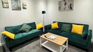 A modern living room with two green sofas, each with yellow cushions, a wooden coffee table, and artwork on the walls. - Contractor/Corporate-Friendly Home | Sleeps 6 | Long Stays (Bolton)