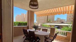 Un'area pranzo all'aperto riparata, con tavolo e sedie, un lampadario e vista su edifici e vegetazione.